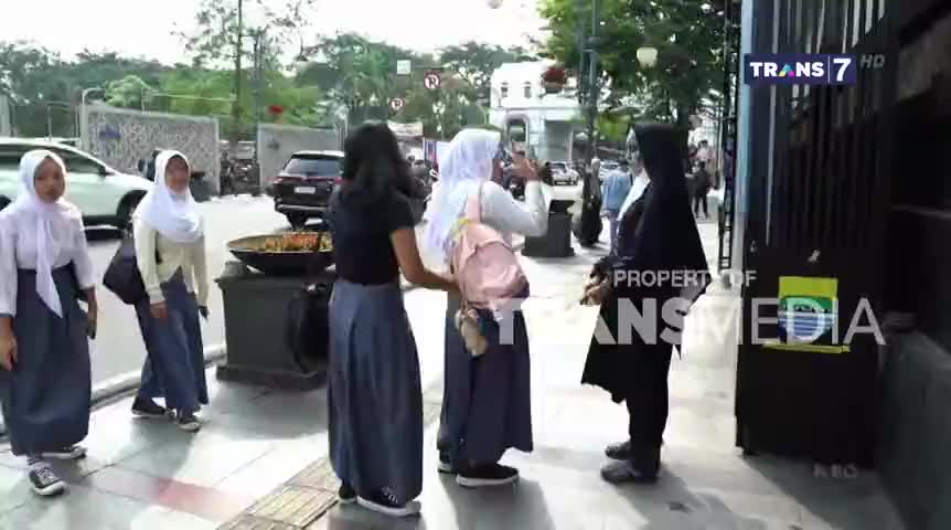 On a sidewalk, several young women in school uniforms are gathered, one taking a photo with her phone. The scene is framed by a "Trans 7" logo, suggesting this is a broadcast from Indonesia.
On a sidewalk, several young women in school uniforms are gathered, one taking a photo with her phone. The scene is framed by a "Trans 7" logo, suggesting this is a broadcast from Indonesia.