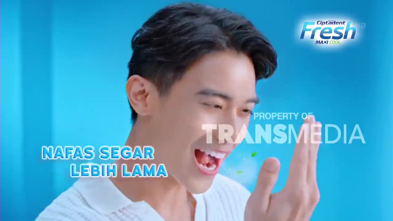 A young man smiles, exhaling a puff of minty air that drifts across his hand. The Trans7 logo is visible on screen, a reminder of where this Indonesian commercial is airing. A young man smiles, exhaling a puff of minty air that drifts across his hand. The Trans7 logo is visible on screen, a reminder of where this Indonesian commercial is airing.
