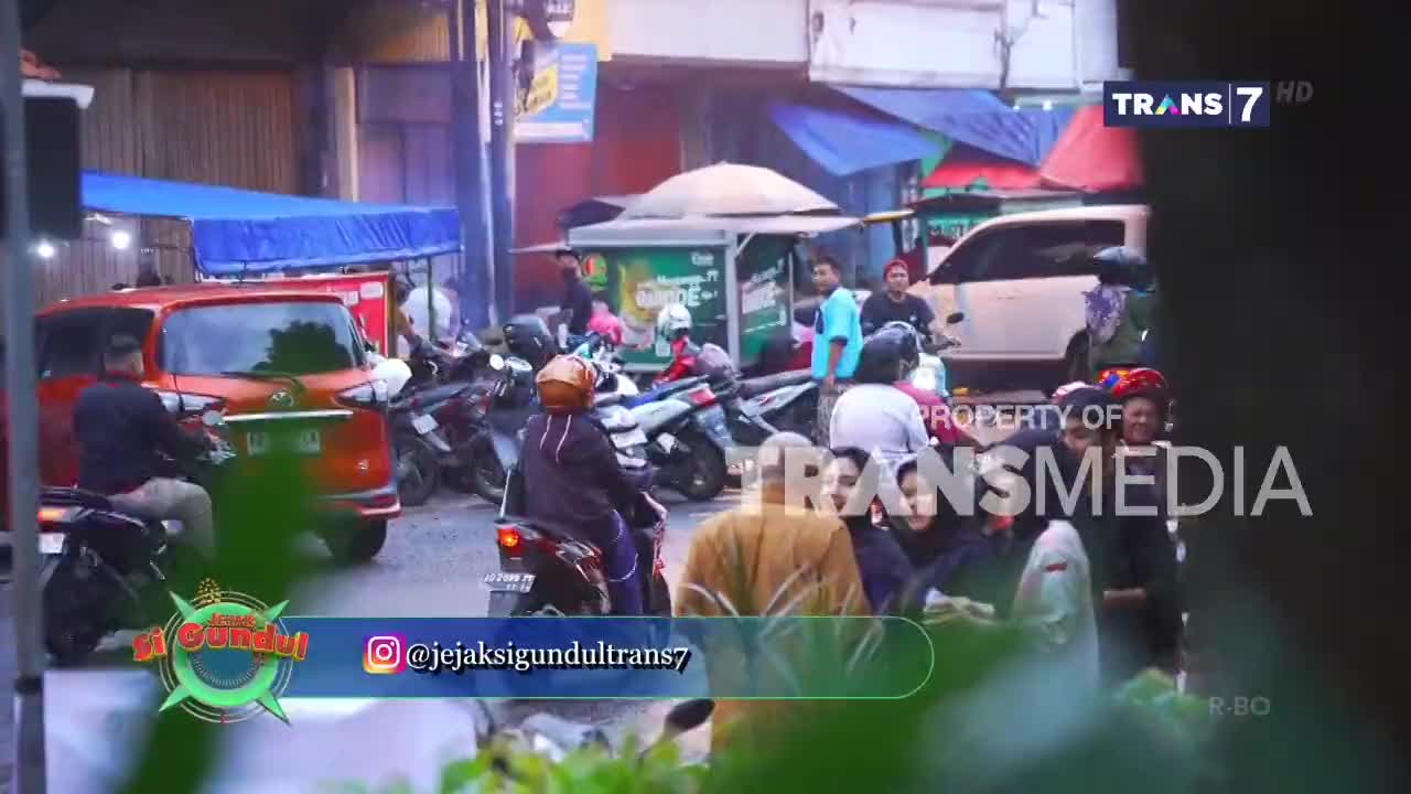 A bright orange car is stopped in traffic, with several motorbikes weaving around it. The sounds of Trans7's "Jejak Petualang" can be heard as people go about their day.