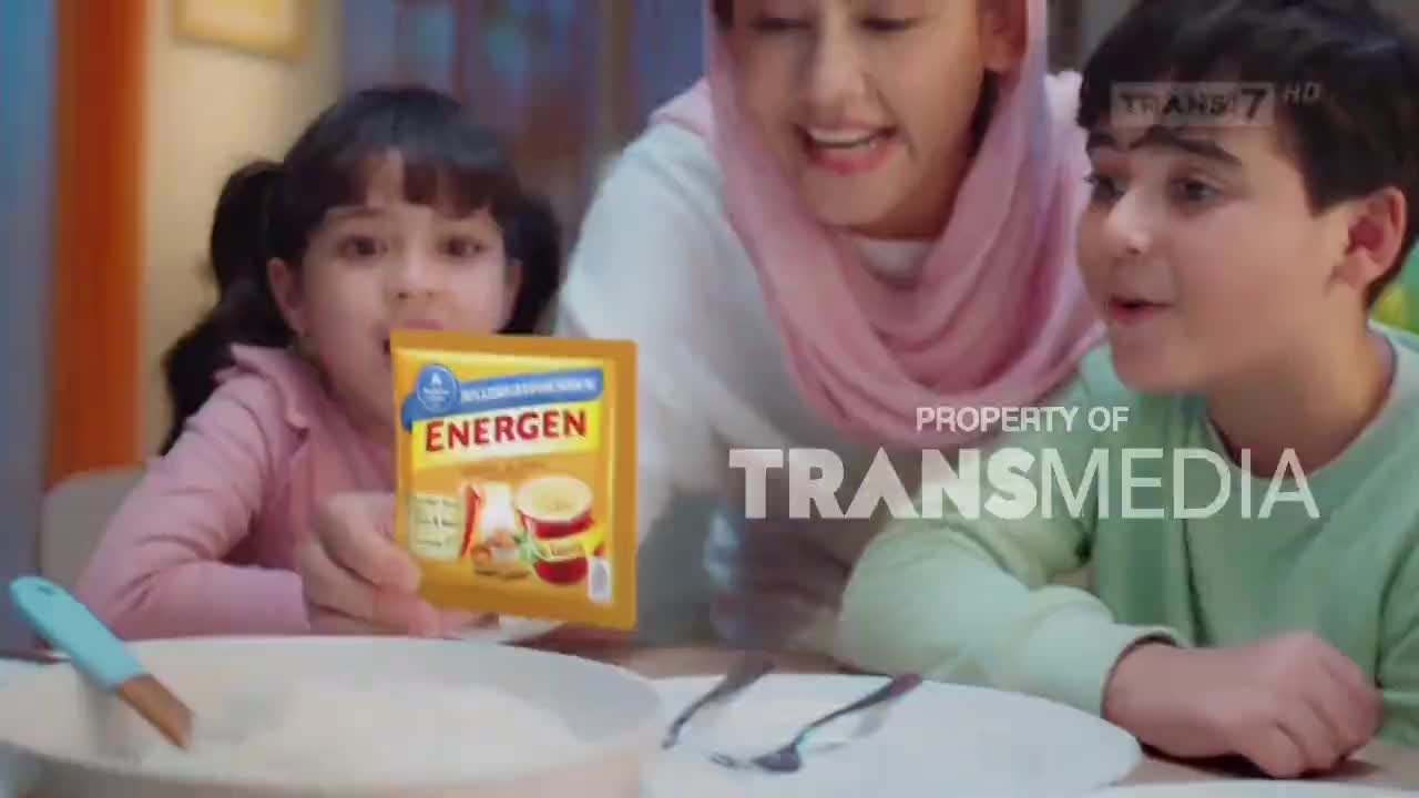 A woman holds up a packet of Energen for two children. The Trans7 logo is visible in the background.