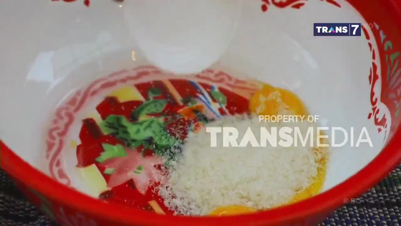 White powder is being sprinkled into a red-rimmed bowl holding egg yolks and chopped ingredients. This preparation is part of a cooking segment on Trans7, a popular Indonesian television channel. White powder is being sprinkled into a red-rimmed bowl holding egg yolks and chopped ingredients. This preparation is part of a cooking segment on Trans7, a popular Indonesian television channel.