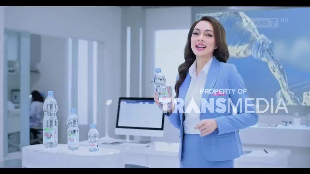 A woman in a blue suit holds a bottle of water, smiling at the camera. Behind her, a large screen displays a graphic of water pouring from a bottle.