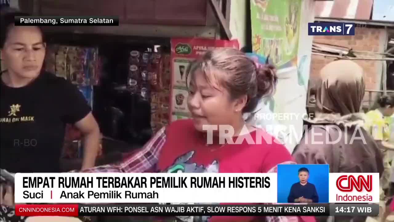 A young woman in a red shirt speaks with a Trans7 reporter, her expression a mix of distress and concern. Behind her, a man in a black shirt looks on, his gaze fixed ahead.