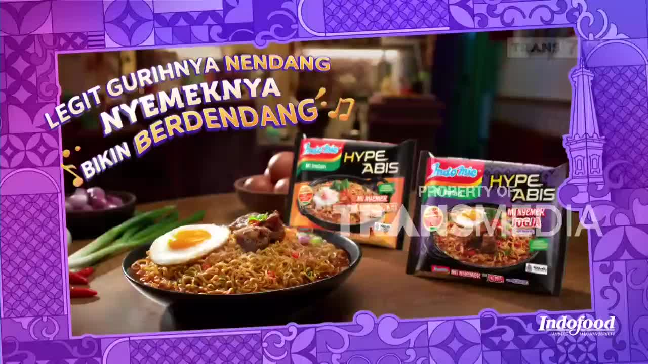 A steaming bowl of Indomie noodles, topped with a fried egg and meat, sits on a table. Two packages of Indomie Hype Abis instant noodles stand behind the bowl, ready to be prepared.