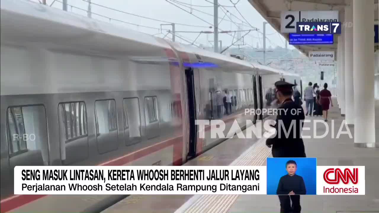 A sleek, white train with red accents glides to a stop at the elevated station. Passengers begin to disembark as a uniformed attendant stands watch on the platform.
