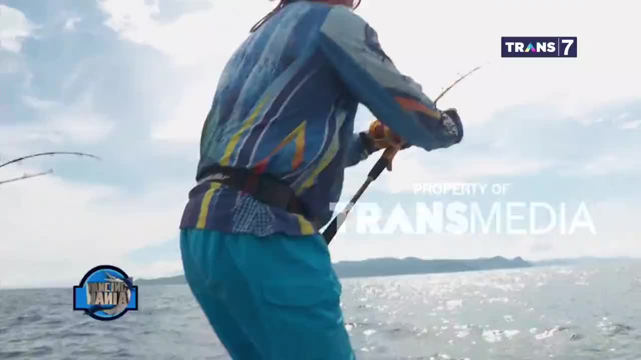 The fishing rod bends sharply as someone on a boat struggles with a catch.  The bright blue sky and choppy water suggest a day out fishing, likely for a show on Trans7.