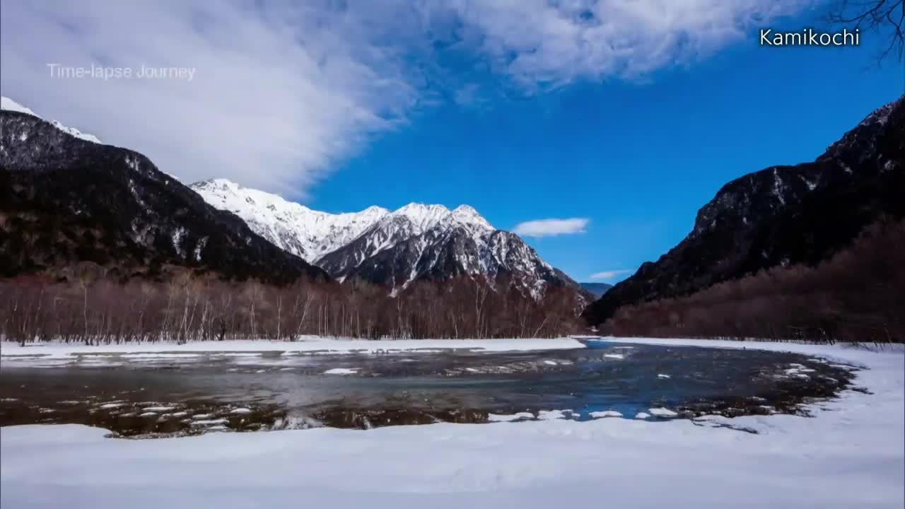 The Japanese Alps tower over a partially frozen river, reflecting the bright blue sky. Patches of snow and ice still cling to the banks, a testament to the lingering winter in Kamikochi, as seen on NHK World-Japan.
