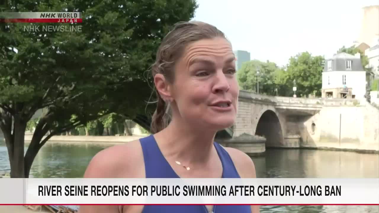 A woman in a blue swimsuit is speaking, likely for an NHK World-Japan news report. Behind her, a stone bridge arches over the Seine River, reflecting the sunny day.
