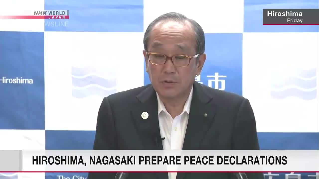 A man in a dark suit and glasses speaks into a microphone, likely for an NHK World-Japan broadcast from Hiroshima. The screen's lower third displays text about peace declarations.
