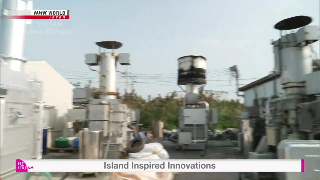 Outside, a series of industrial-looking structures stand in the sunlight, possibly part of an innovation project featured on NHK World-Japan. The tops of these machines have round, flat lids and look like they might be venting something.
