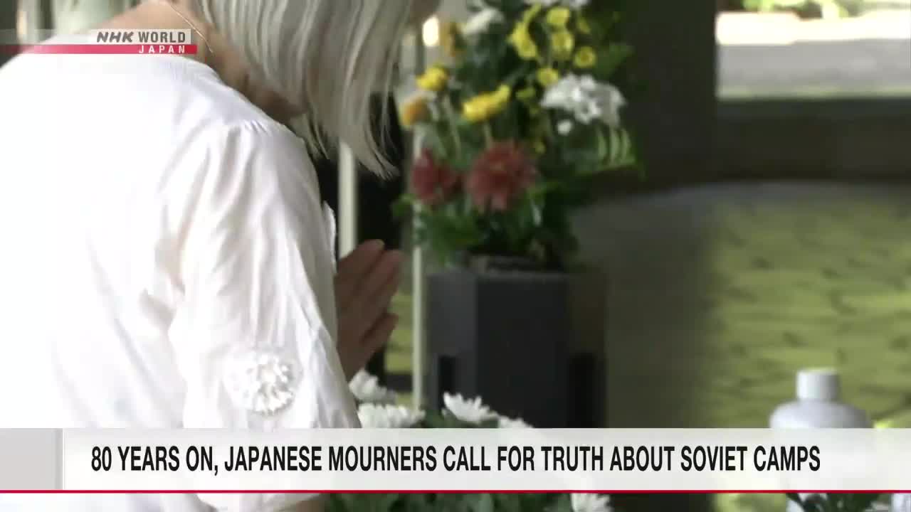 A woman in white, her hands clasped in prayer, bows towards a floral arrangement. NHK World-Japan's coverage highlights the solemn occasion.
