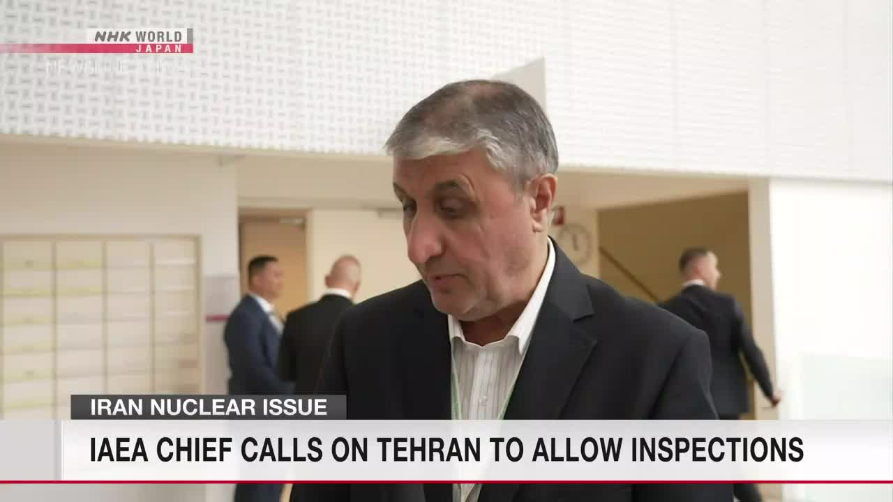 A man in a dark suit speaks, his gaze directed downward. Behind him, other men in suits walk down a hallway, as reported by NHK WORLD-JAPAN.
