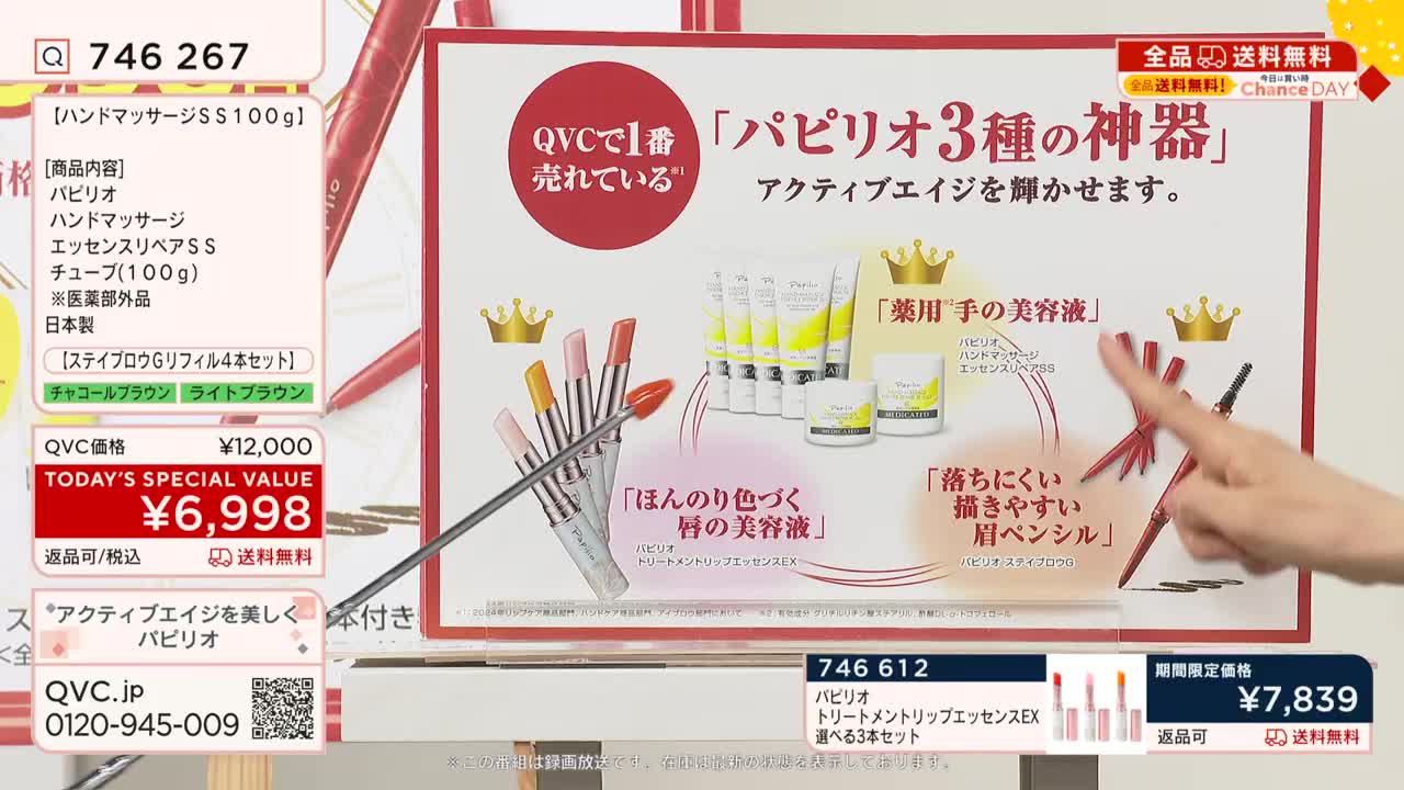 A presenter in Japan is pointing a long, thin rod at a display of beauty products, highlighting a lipstick. The QVC logo and a special price are visible in the corner.
