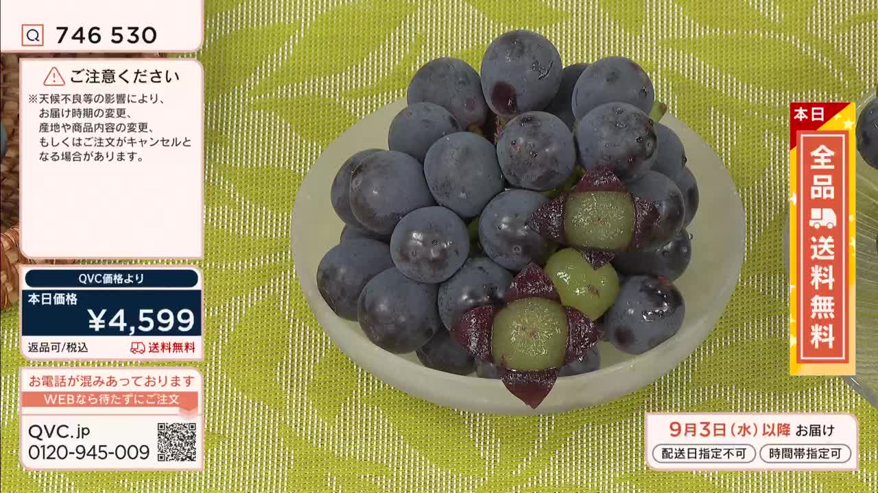 A bowl of dark grapes sits on a patterned green surface, with a few cut open to reveal their pale green insides. The price of these grapes, ¥4,599, is displayed on the QVC screen, along with a note about potential delivery changes.
