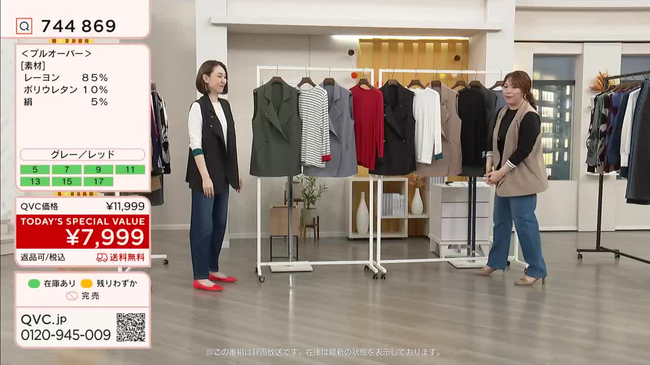 Two women stand in a brightly lit studio, gesturing at a rack of clothing. On a screen, the QVC price for a pullover is displayed in Japanese yen.
