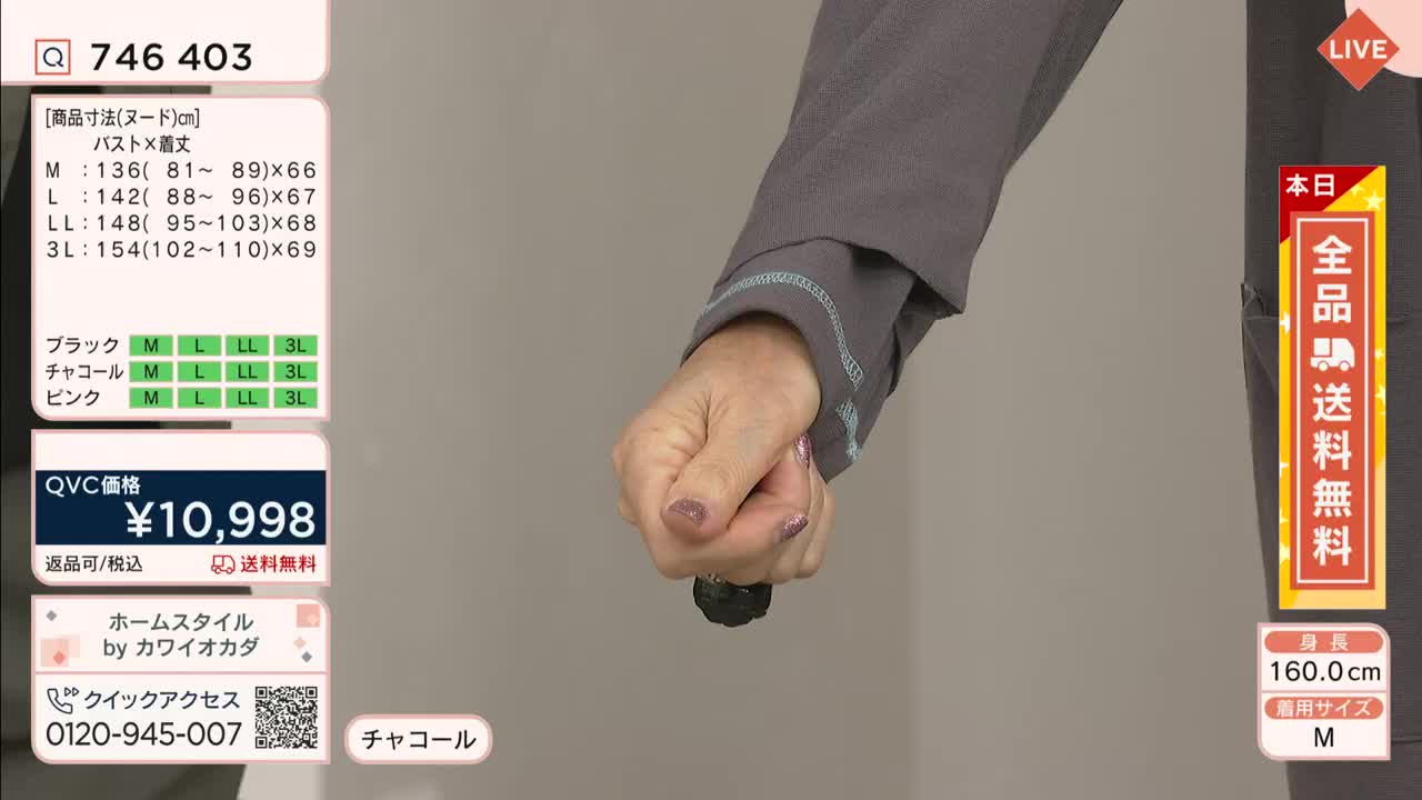 A woman's hand, clad in a gray sleeve, grips a small, dark object. The QVC price tag and product details are displayed on the screen behind her.
