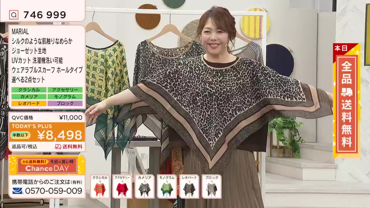 A woman on a QVC-style show in Japan is demonstrating a leopard-print scarf.  She's holding her arms out to show the garment's shape, smiling directly at the camera.
