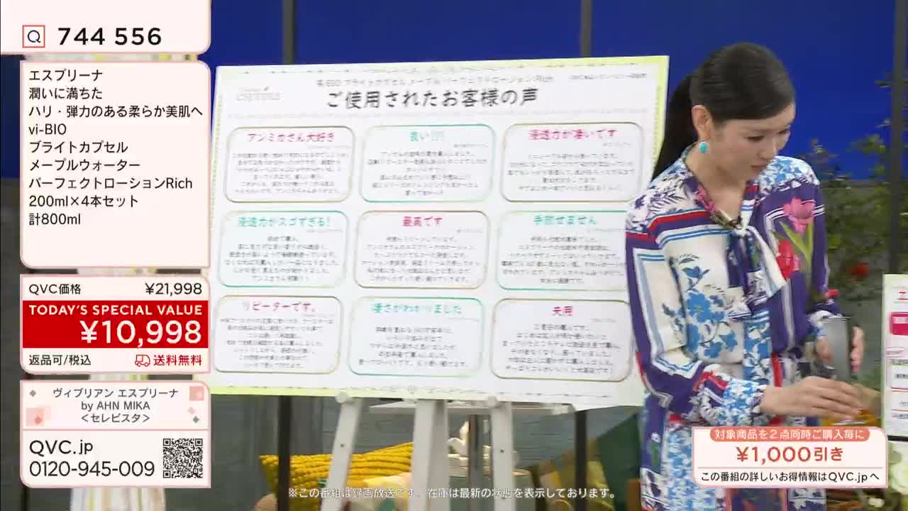 A woman in a floral dress stands next to a large whiteboard covered in Japanese text, holding a small, silver bottle. The screen displays a special offer from QVC Japan.
