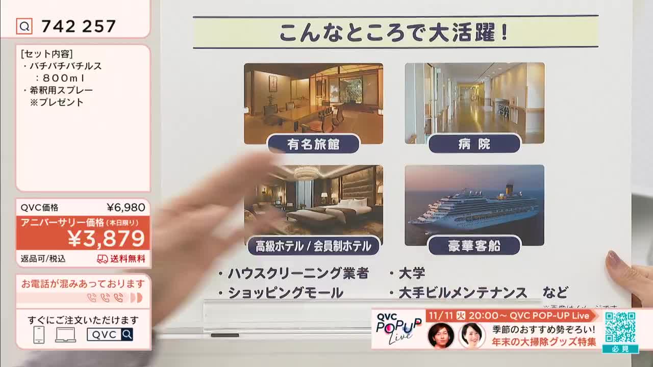 A hand gestures across a screen showing images of hotels, a cruise ship, and a hospital, advertising a cleaning product on QVC Japan. The price is highlighted in red, with a special anniversary discount for today only.
