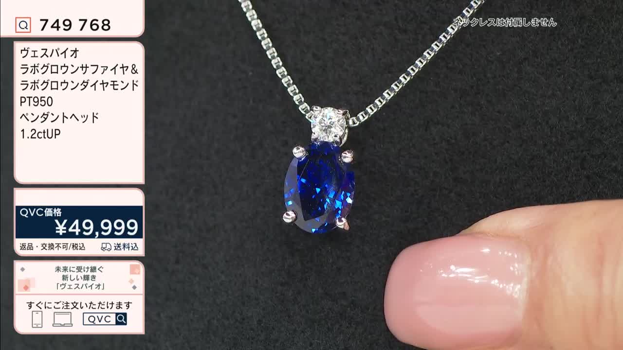 A hand gently displays a sapphire pendant, its deep blue contrasting with the bright diamond above. The QVC price of ¥49,999 is visible alongside the product details in Japanese.
