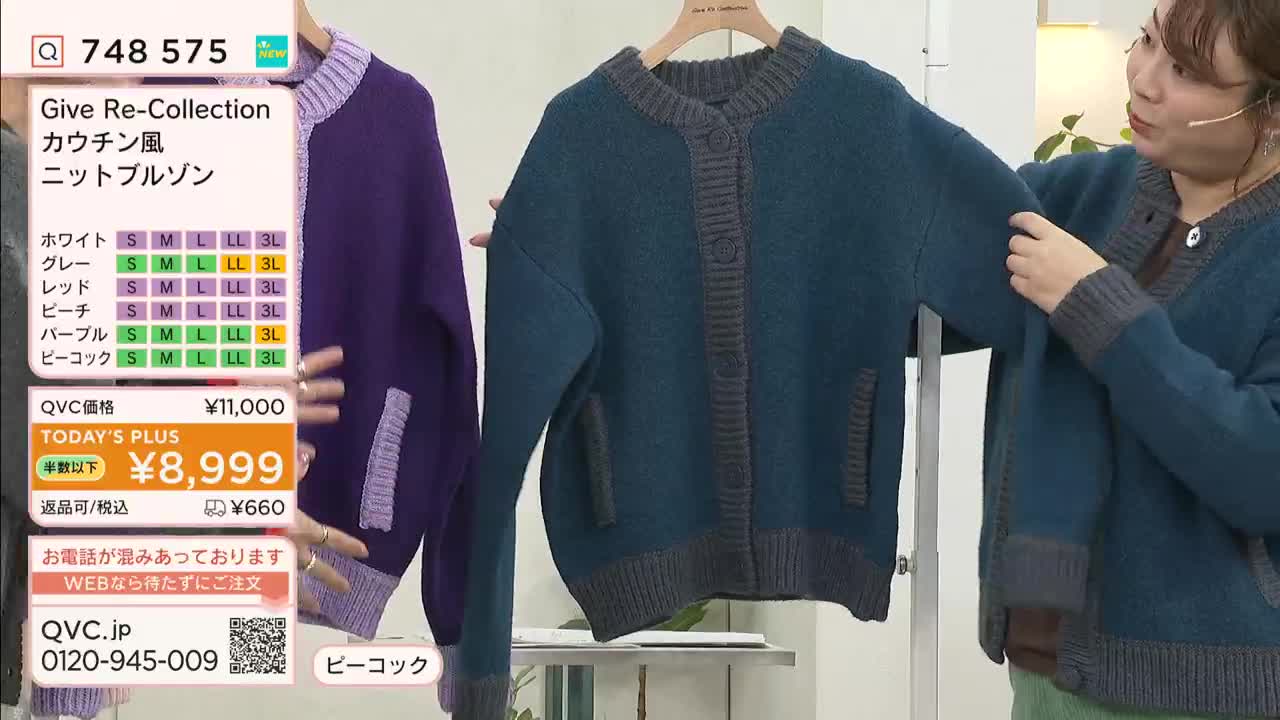 A woman on a QVC-style broadcast in Japan holds up a teal cardigan, pointing out the sleeve detail. Beside her, a purple version of the same sweater hangs on a rack.
