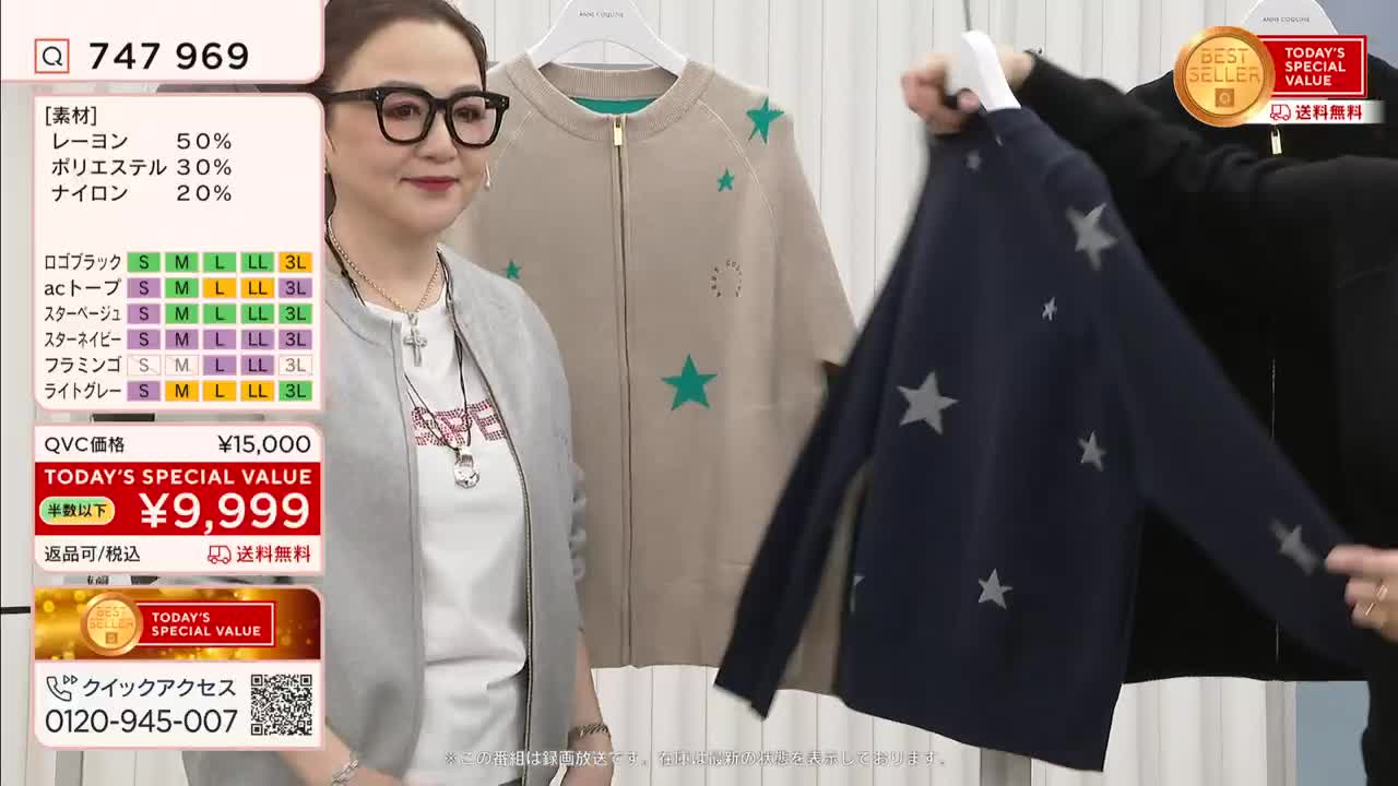 A woman in glasses smiles at the camera while another person holds up a navy blue cardigan decorated with gray stars. Behind them, a beige cardigan with green stars hangs on a rack, all part of a QVC Japan presentation.
