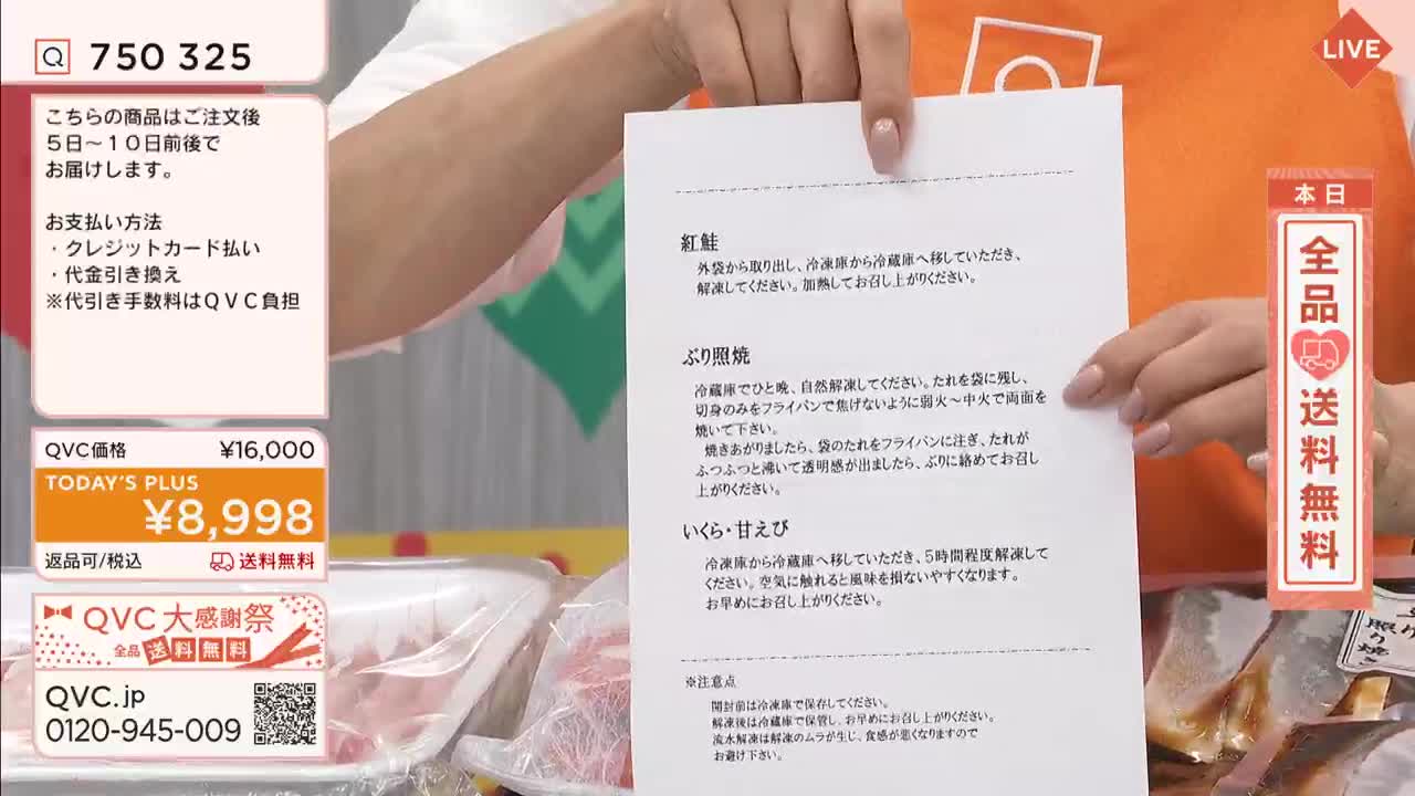 A presenter on QVC in Japan holds a sheet of paper, likely a recipe or product description, for the camera. The paper lists instructions for preparing frozen seafood, including salmon, grilled yellowtail, and shrimp roe.
