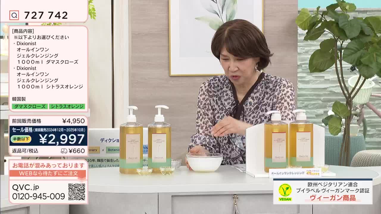 A woman on a QVC broadcast in Japan is demonstrating a cleansing product. She gestures towards a bowl of white liquid as large bottles of the product sit on display. A woman on a QVC broadcast in Japan is demonstrating a cleansing product. She gestures towards a bowl of white liquid as large bottles of the product sit on display.