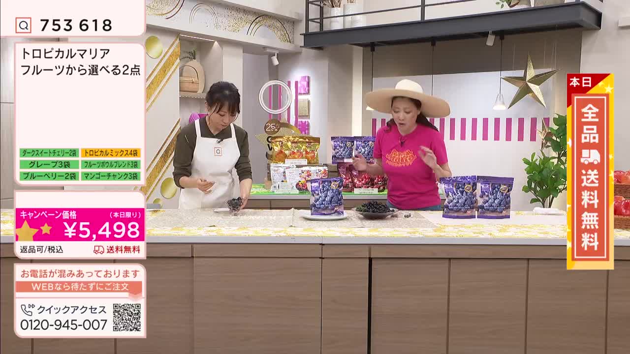 A woman in a bright pink shirt and wide-brimmed hat gestures enthusiastically, showcasing bags of blueberries on a QVC broadcast. Beside her, another woman in an apron carefully handles a small pile of the dark berries.