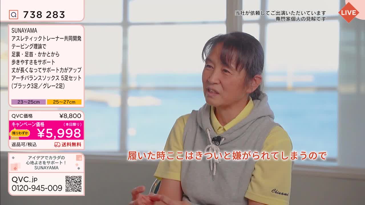 A woman with short, dark hair speaks animatedly, her hands gesturing slightly. Text overlays in Japanese indicate a QVC broadcast, featuring a product called "Arch Balance Socks."