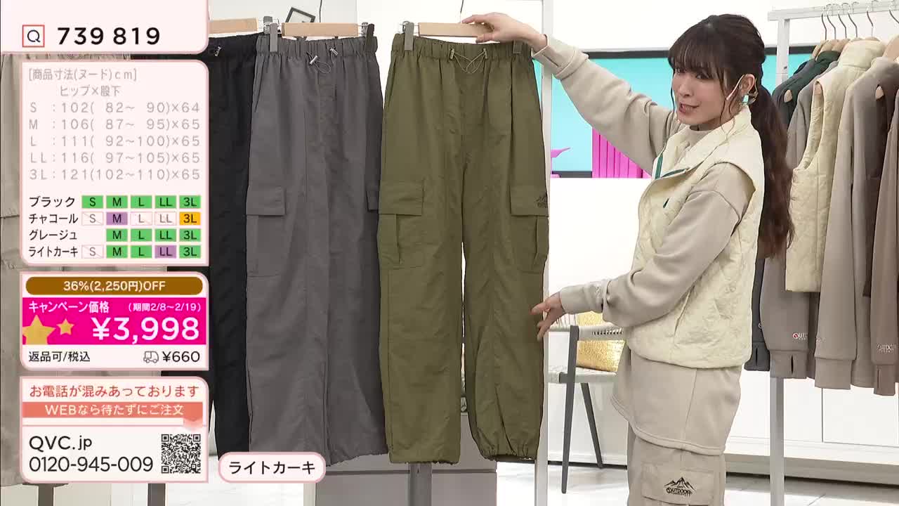 A woman on a QVC broadcast in Japan holds up a pair of olive green cargo pants. She gestures towards the fabric as she presents the item. A woman on a QVC broadcast in Japan holds up a pair of olive green cargo pants. She gestures towards the fabric as she presents the item.