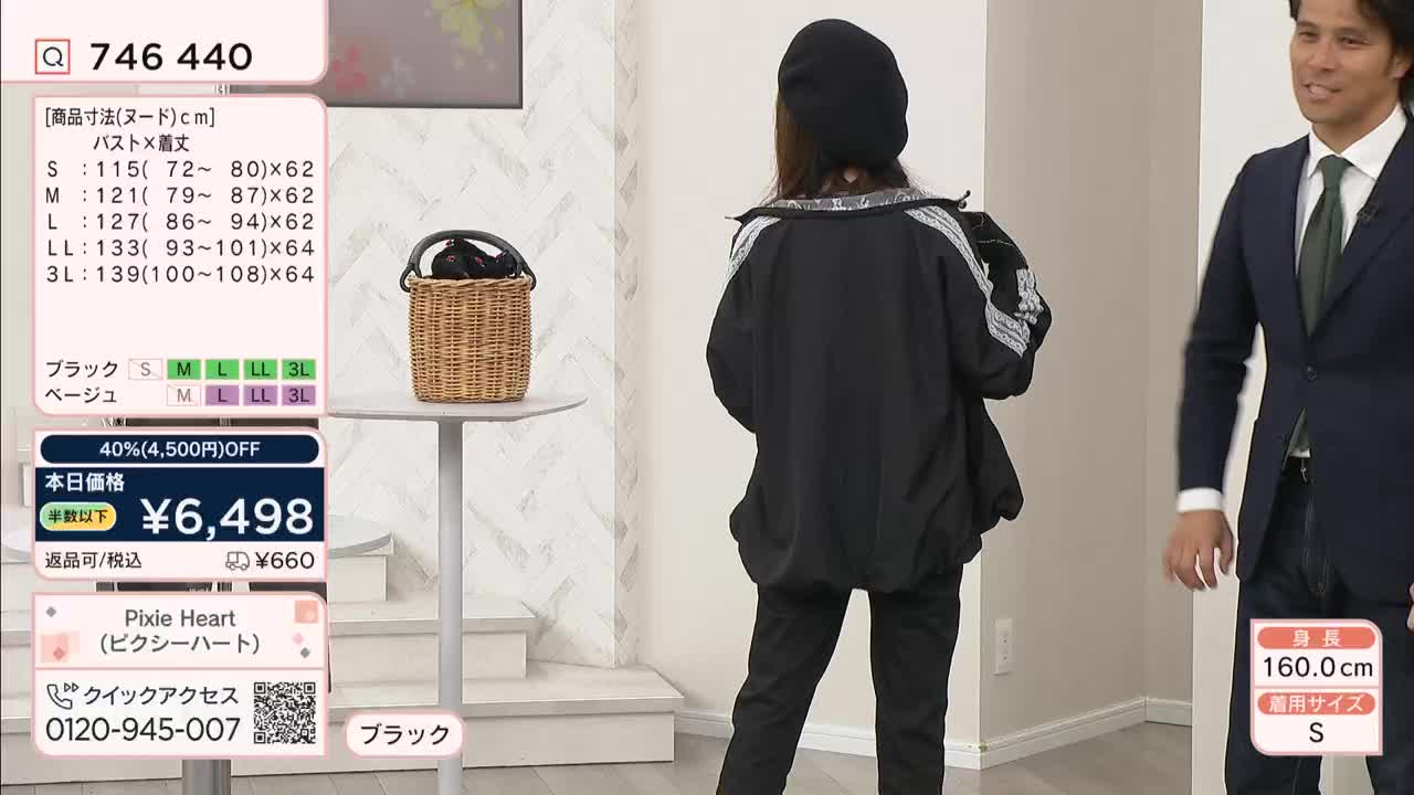 A woman in a black beret and jacket stands facing away, while a man in a suit smiles to her right. On the left, a QVC-style graphic displays product information.