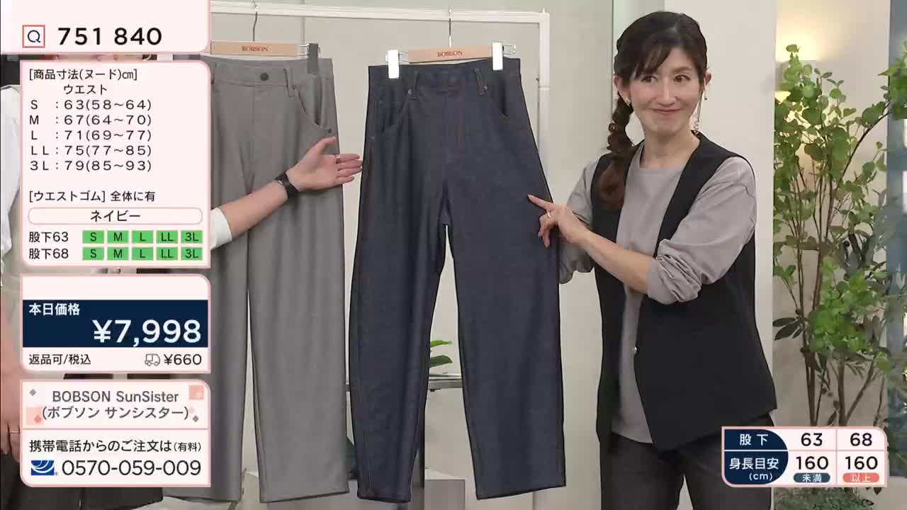 A woman gestures towards a pair of dark, wide-leg trousers hanging on a rack. Another person's hand points to a gray pair of pants next to them.