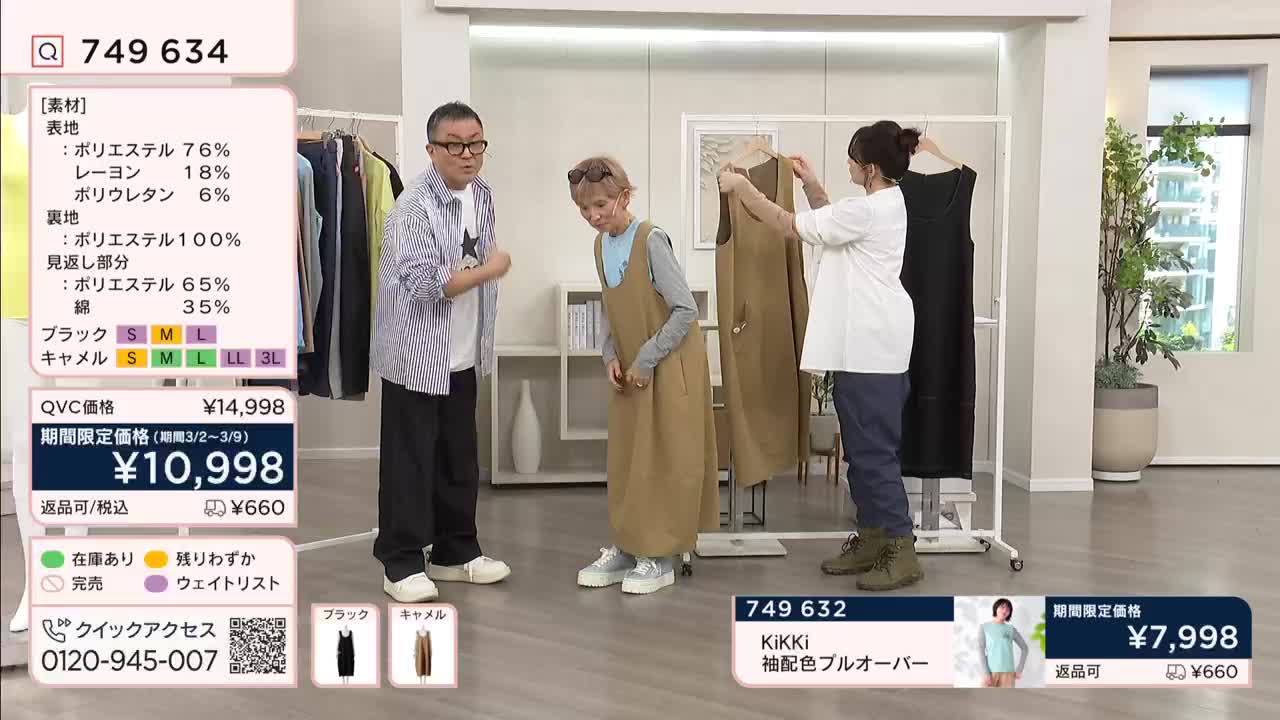 A woman holds up a tan dress for inspection while another woman, wearing a similar style, stands nearby. A man in a striped shirt watches them, gesturing with his hands.