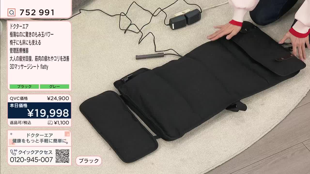 Hands smooth out a black massage mat on a rug. The mat is connected to a power cord and a small control unit.