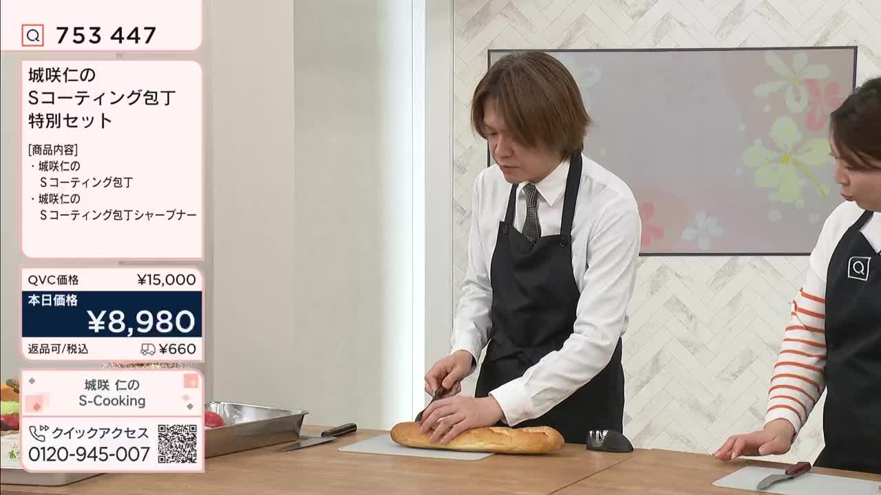 A man in an apron carefully slices a baguette on a cutting board. Beside him, a woman watches, her hands resting on the counter.