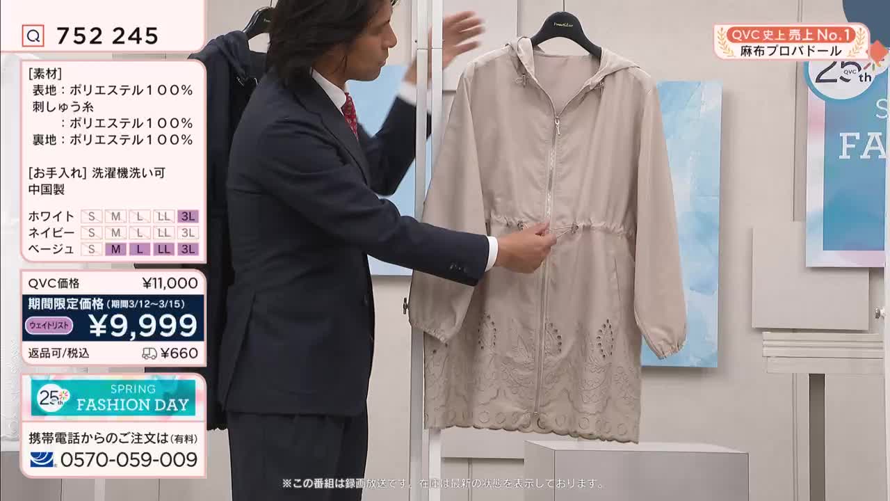 A man in a suit adjusts the drawstring on a light beige jacket. The jacket hangs on a display, showcasing its delicate embroidered hem.