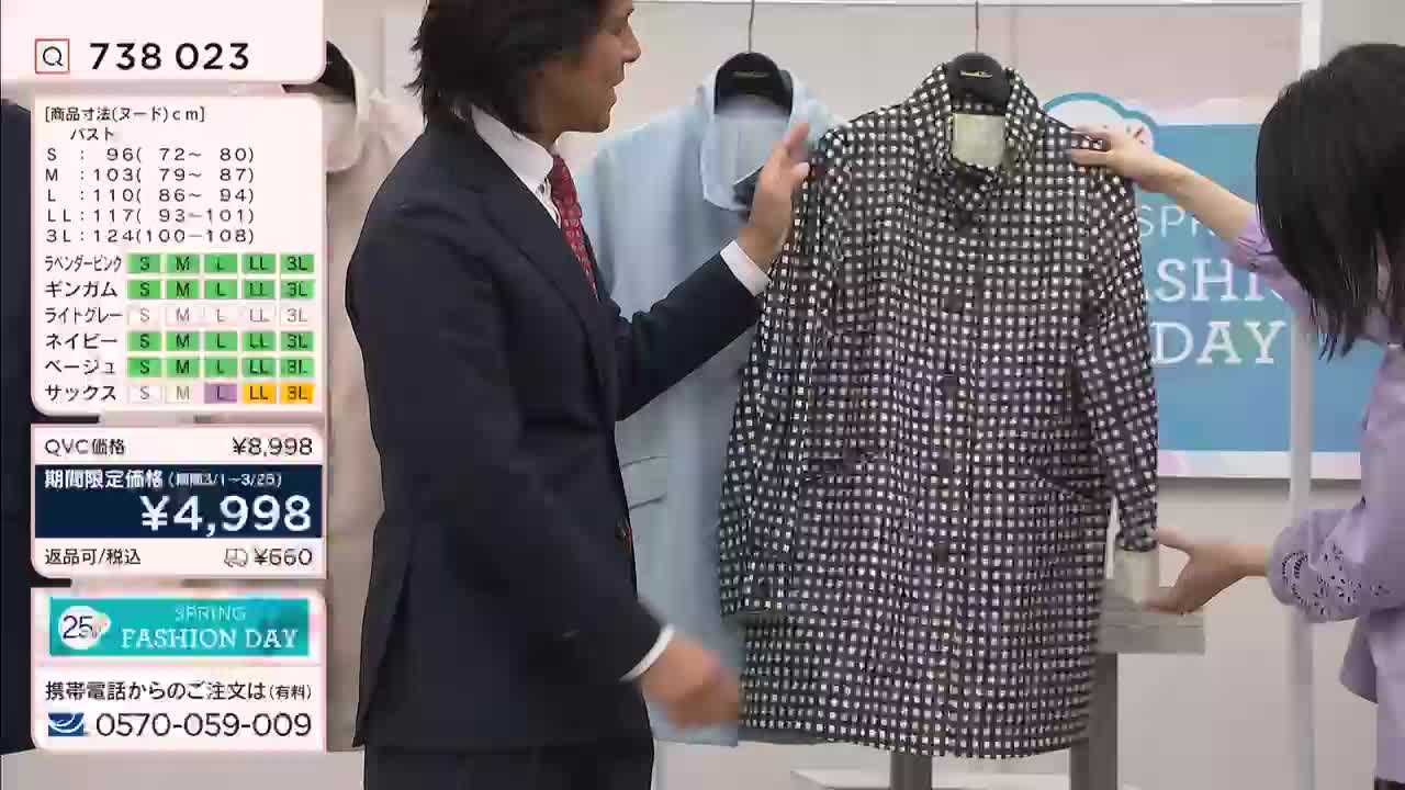 A man in a suit gestures towards a black and white checkered jacket, while a woman in a lavender top adjusts its sleeve. A pale blue coat hangs behind them.