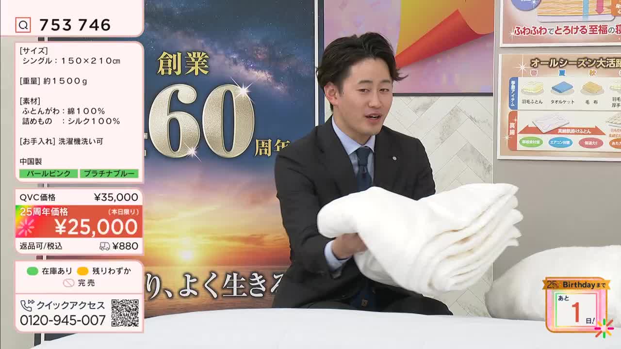 A man in a suit holds up a neatly folded white comforter. He's on a QVC broadcast, likely in Japan, showcasing bedding.