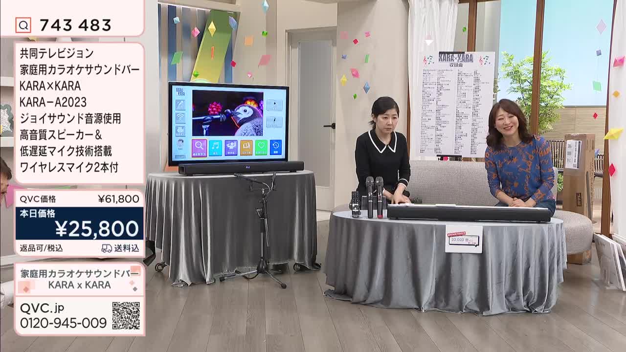 Two women are presenting a karaoke soundbar on QVC Japan. A large television displays a penguin singing, and microphones sit on a table.