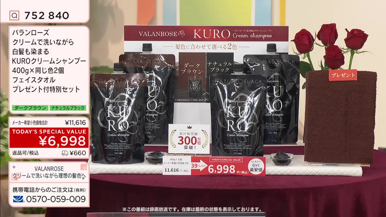 A display of KURO Cream Shampoo stands ready for sale on QVC Japan, with pouches of dark brown and natural black shades arranged behind a small award. A folded brown towel, adorned with a "Present" tag and topped with red roses, sits to the right of the shampoo display.