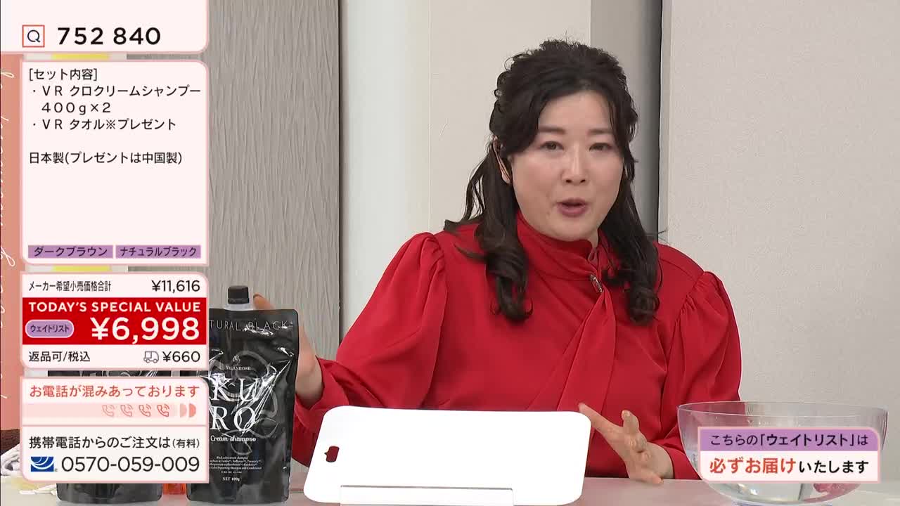 A woman in a bright red top gestures enthusiastically while holding up a black pouch. On a screen behind her, Japanese text displays product details and a phone number for ordering. A woman in a bright red top gestures enthusiastically while holding up a black pouch. On a screen behind her, Japanese text displays product details and a phone number for ordering.