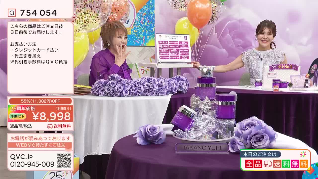 A woman in a purple top gestures animatedly while a second woman in a sparkly top smiles and holds up a tablet. The table between them is covered in purple fabric and adorned with ornate purple jars and faux roses. A woman in a purple top gestures animatedly while a second woman in a sparkly top smiles and holds up a tablet. The table between them is covered in purple fabric and adorned with ornate purple jars and faux roses.
