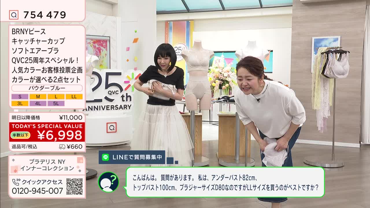 A woman in a black top and white skirt adjusts a white garment she's holding. Another woman in a white shirt and jeans leans forward, smiling.