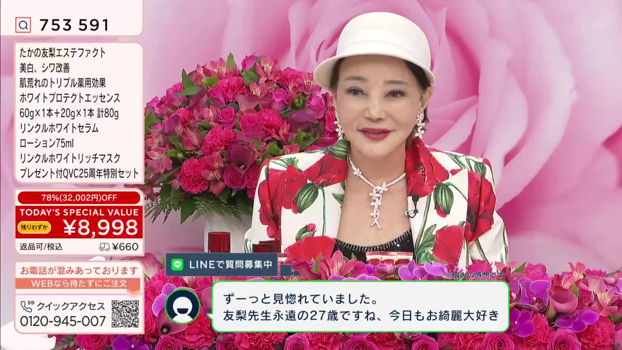 A woman in a floral jacket and white hat smiles, her jewelry catching the light. Behind her, a QVC broadcast displays product details and a price of ¥8,998.