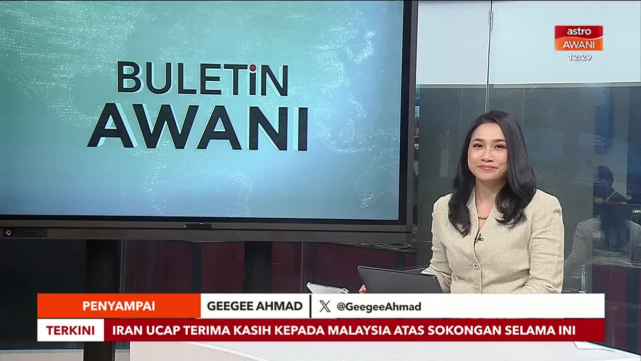 In a Malaysian studio, Geegee Ahmad smiles at the camera, ready to deliver the news on Astro Awani. Behind her, the screen displays "BULETIN AWANI," and a headline about Iran's gratitude to Malaysia scrolls across the bottom.
