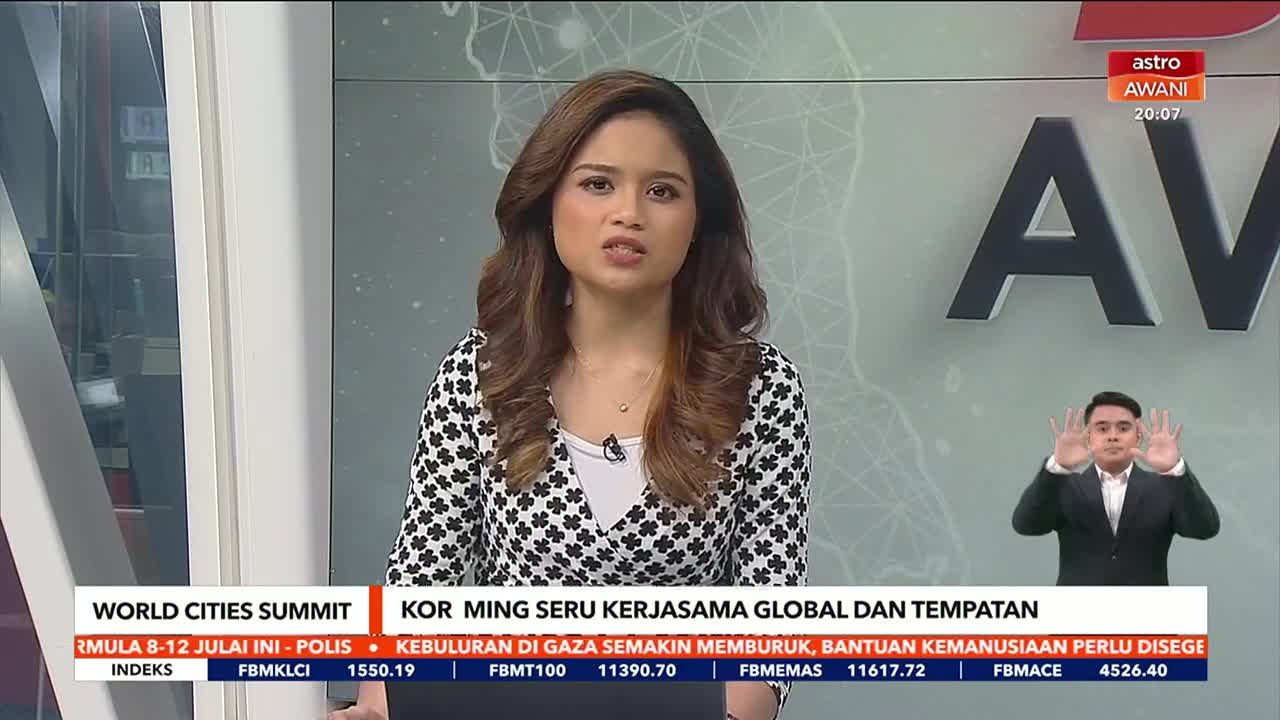 A woman in a patterned top speaks directly to the camera on Astro Awani, with a sign language interpreter visible in the lower right. The backdrop features a map and the channel's logo.
