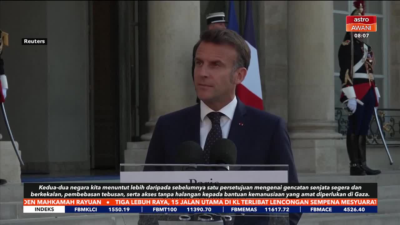 A man in a dark suit speaks at a podium, the French flag behind him. The Astro Awani logo is in the upper right corner, and text crawls across the bottom of the screen.
