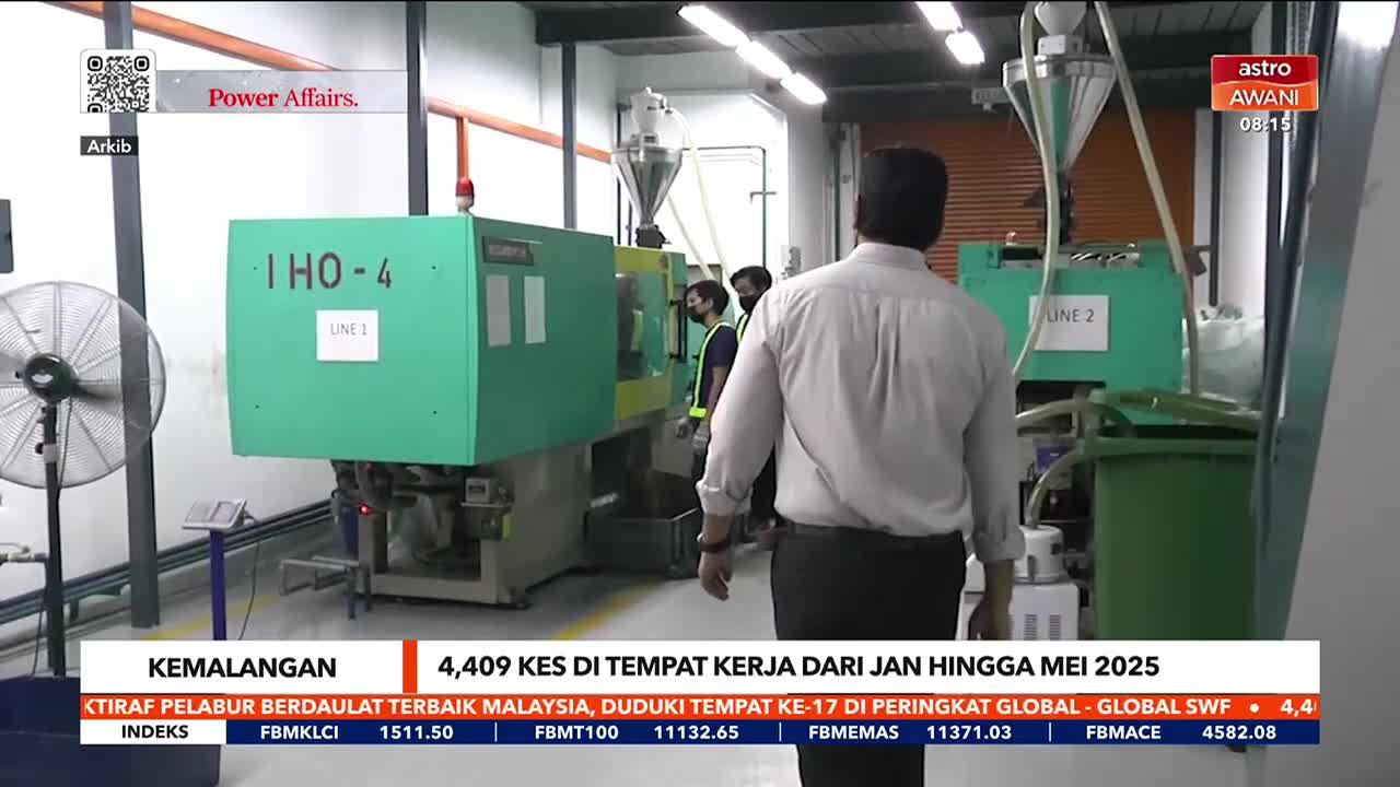 A man in a white shirt walks past large green machines, labeled "Line 1" and "Line 2." The Astro Awani logo is visible in the corner, and a news ticker at the bottom displays information about workplace accidents in Malaysia.
