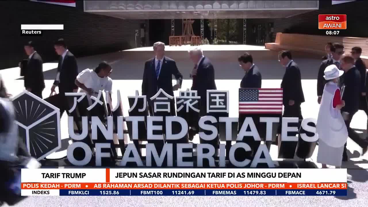 A group of people in suits and a woman in a white hat walk past a large sign that spells out "UNITED STATES OF AMERICA" in front of a building. The Astro Awani logo is in the top right corner, and the bottom of the screen displays headlines in Malay.

